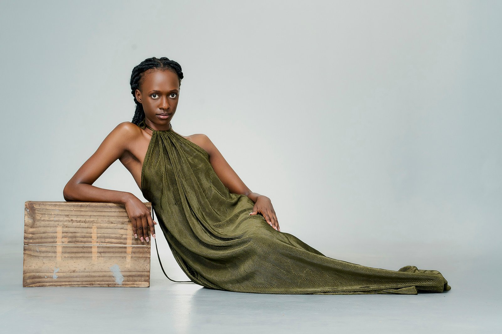 A model in a long green dress leaning on a wooden box